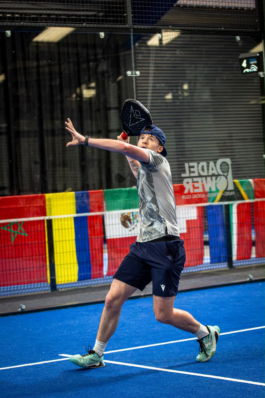 A coach striking the ball at a padel tournament